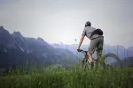 Person fährt Fahrrad in einem Grasbereich mit Bergen im Hintergrund