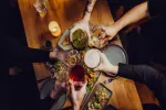 Hände stoßen über einem Tisch mit verschiedenen Gerichten an