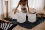 Person mit Kristallschalen und verschiedenen Instrumenten auf einer Matte