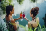 Zwei Frauen halten Cocktails am Wasser.