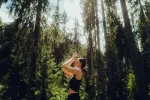 Person macht Yoga zwischen hohen Bäumen im Wald