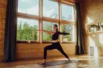 Frau übt Yoga in einem Holzraum mit großen Fenstern