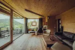 Innenansicht einer Holzblockhütte mit großen Fenstern und einem Sofa
