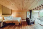 Gemütlicher Holzraum mit Bett, Sofa und großen Fenstern
