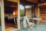 Innenansicht einer Holzkabine mit Bett und Stühlen auf der Veranda