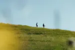 Zwei Personen gehen auf einem grasbewachsenen Hügel unter klarem Himmel