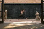 Person tanzt neben einer Steinmauer mit Skulpturen