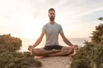 Mann, der bei Sonnenuntergang am Strand meditiert