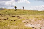 Zwei Personen gehen auf einem grasbewachsenen Hügel unter Wolken