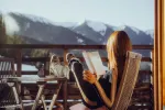 Person liest auf einer Terrasse mit Bergen im Hintergrund
