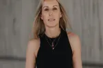 Frau mit langen Haaren in schwarzem Top vor grauem Hintergrund