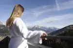 Person in einem Bademantel, die die Berglandschaft von einem Balkon aus genießt
