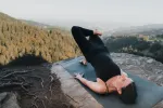 Person macht Yoga auf einem felsigen Untergrund mit Bergen