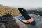 Person macht Yoga auf einer Matte mit Aussicht auf Berge