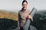 Frau hält eine Yogamatte im Freien mit Bergen im Hintergrund