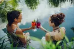 Zwei Frauen stoßen mit Cocktails am Wasser an