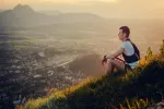Person sitzt auf einem Hügel mit Blick auf ein Tal bei Sonnenuntergang