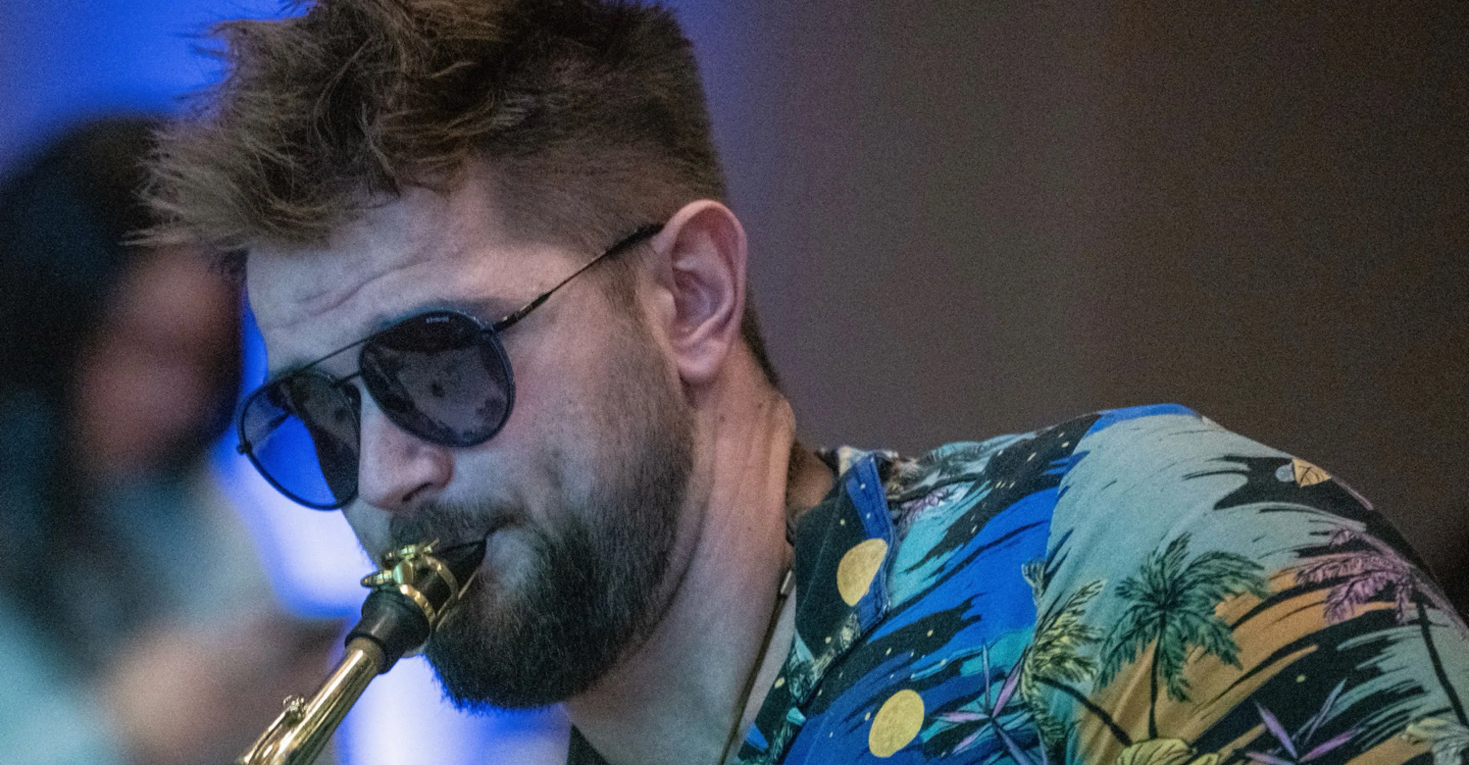 Mann mit Sonnenbrille spielt Saxophon, farbenfrohe Hemd