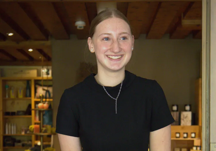 Junge Frau in einem Geschäft lächelt, Regale mit Produkten im Hintergrund.