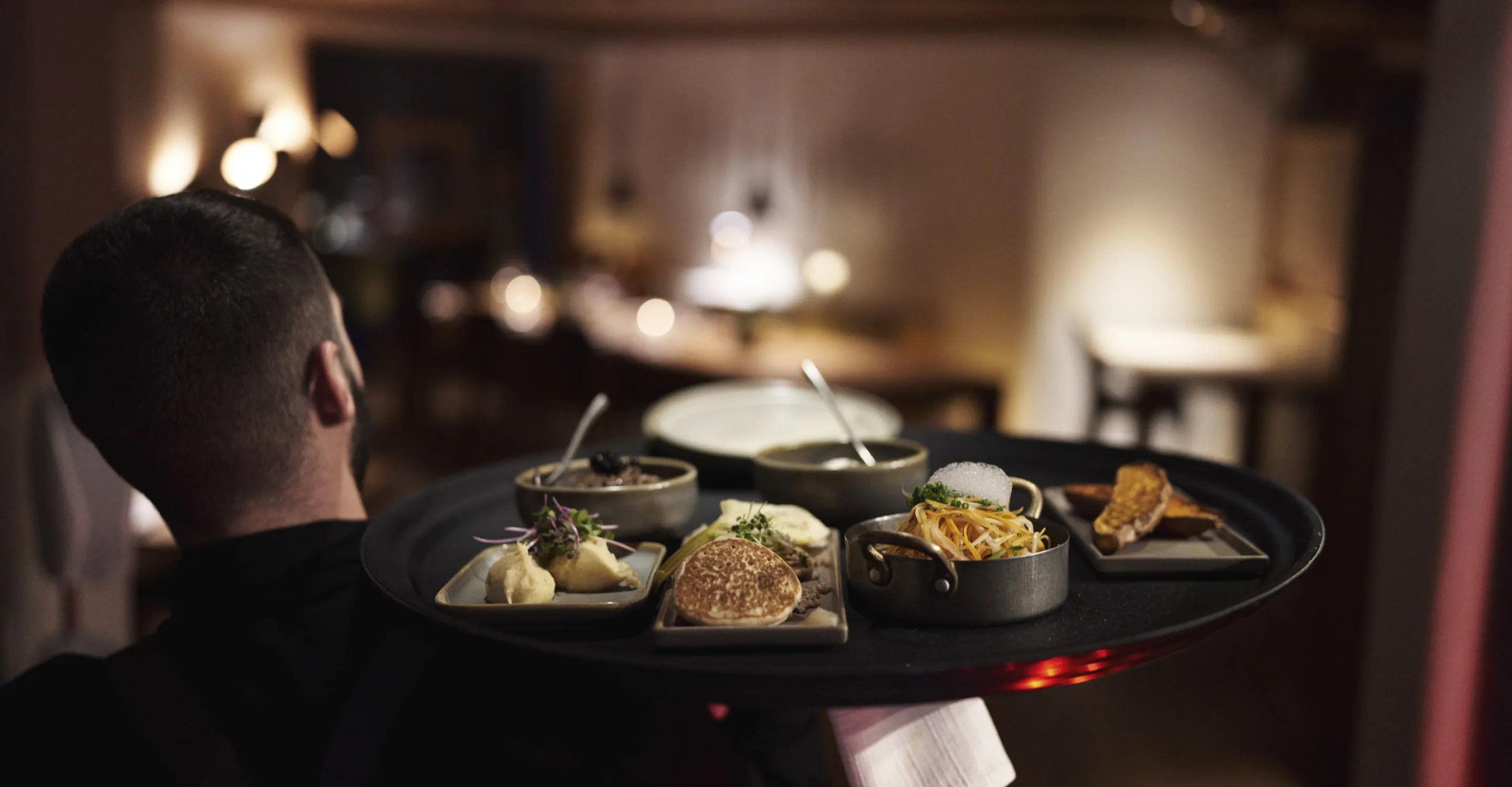 Kellner trägt Gerichte im Holzhotel Forsthofalm.