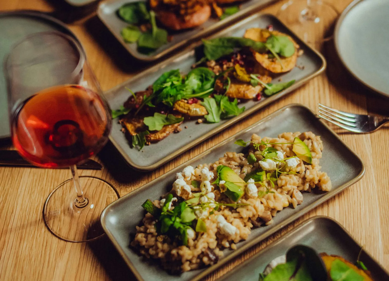 Teller mit Risotto und Salat sowie einem Glas Rotwein auf einem Holztisch