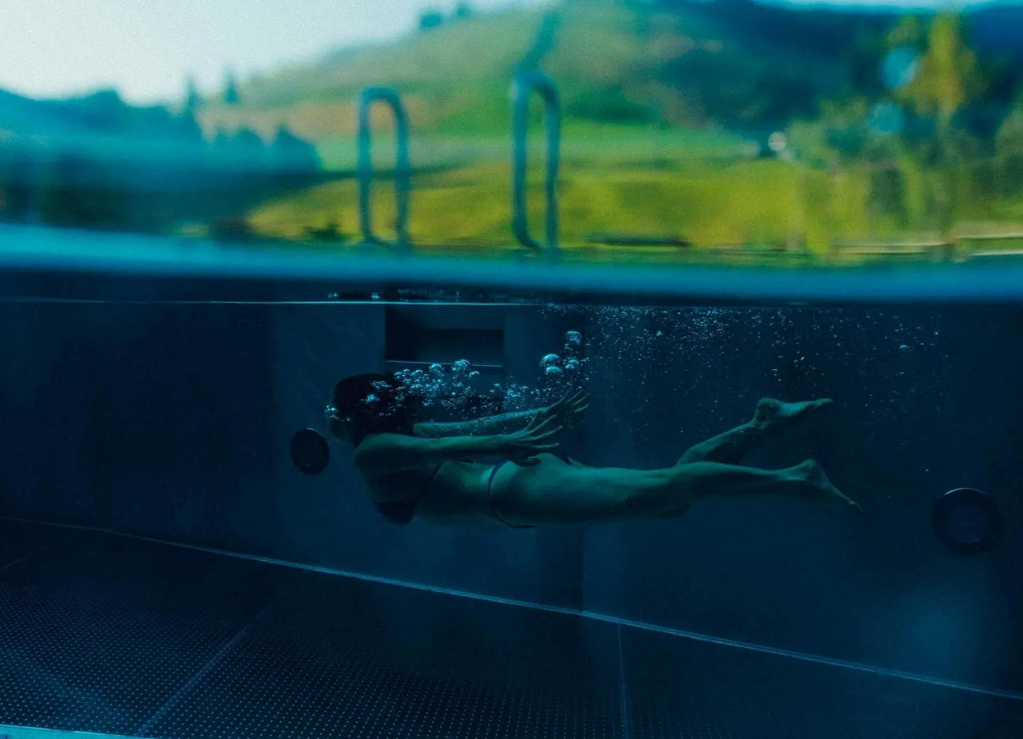 Eine Person schwimmt unter Wasser in einem Pool mit einem Blick auf die Landschaft.