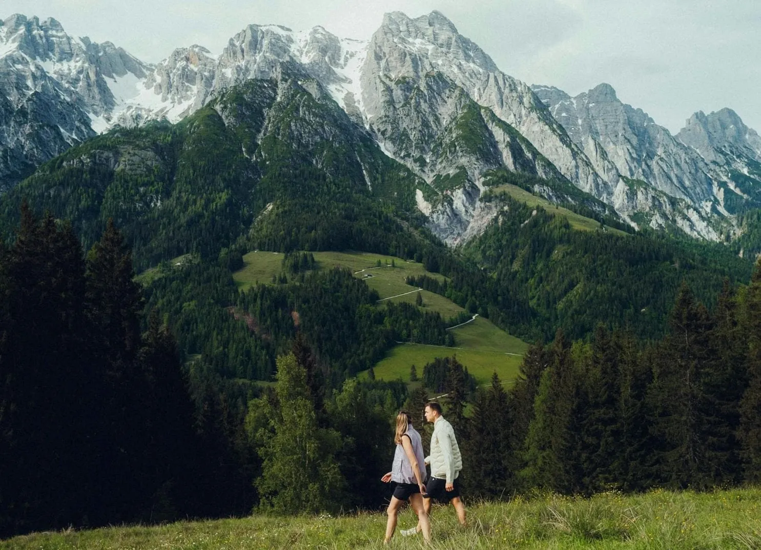Zwei Personen, die durch ein grünes Feld mit Bergen im Hintergrund gehen