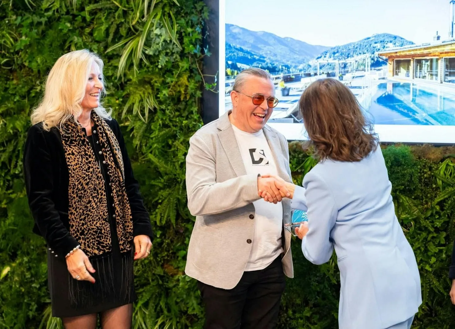 Drei Personen, eine shakehands vor einem Bildschirm mit Landschaftsbild.