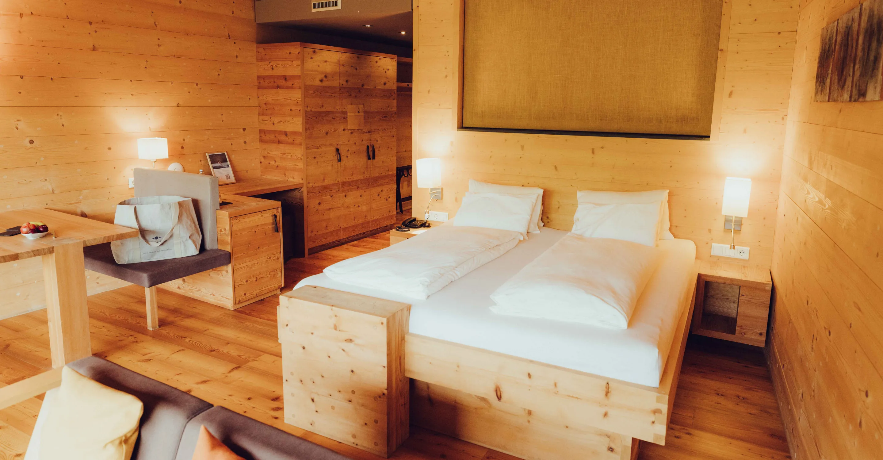 Helles Zimmer mit Holzverkleidung, Doppelbett und Arbeitsbereich.