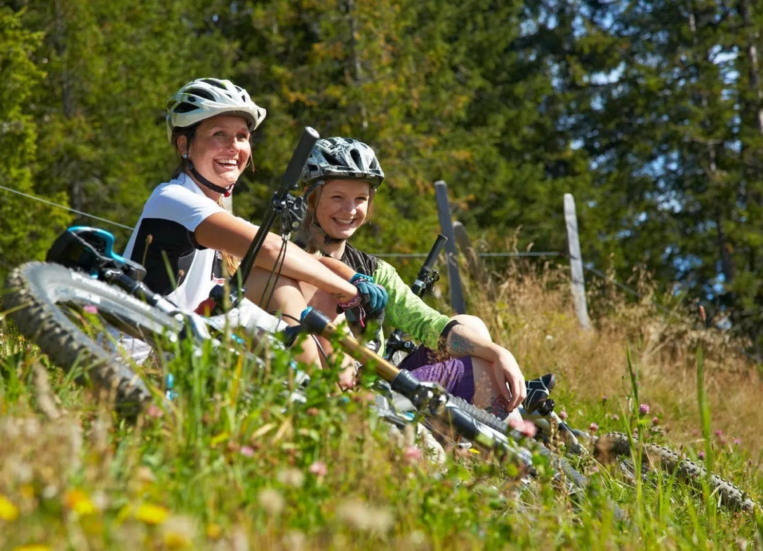 Zwei lächelnde Radfahrer, die auf einem grasbewachsenen Hügel mit Fahrrädern in einem Waldgebiet pausieren