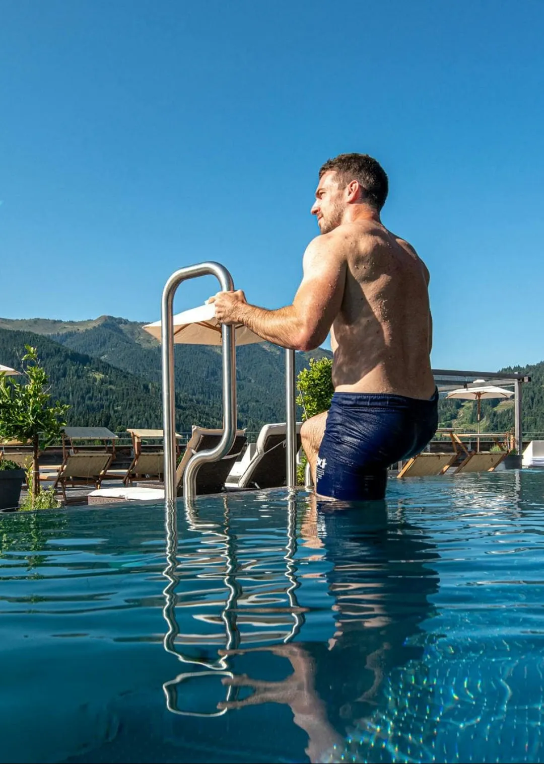 Mann steigt aus einem Pool mit Blick auf Berge und Sonnenliegestühle