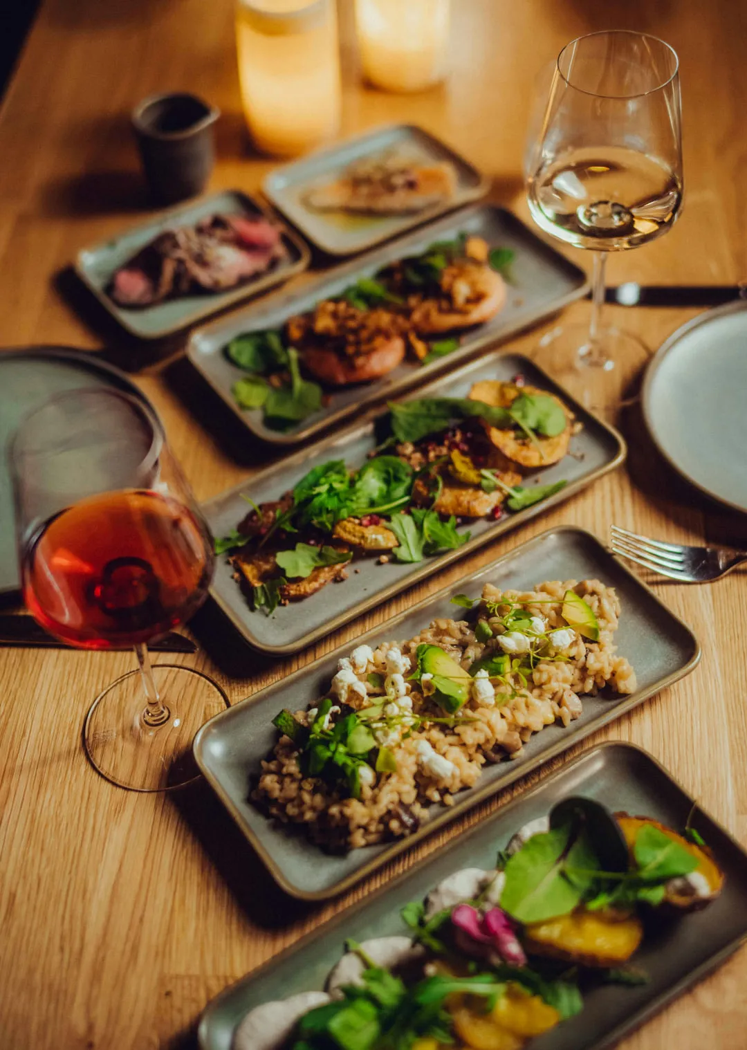 verschiedene Gourmetspeisen auf einem Holztisch mit Getränken und Kerzen