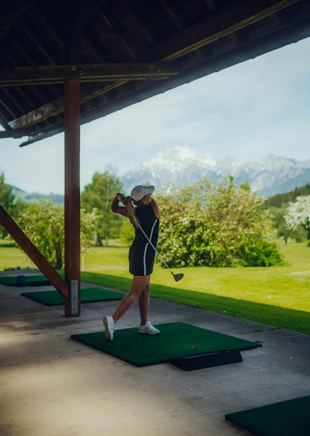 Frau schlägt Golfball auf einer Driving Range mit Bergen im Hintergrund
