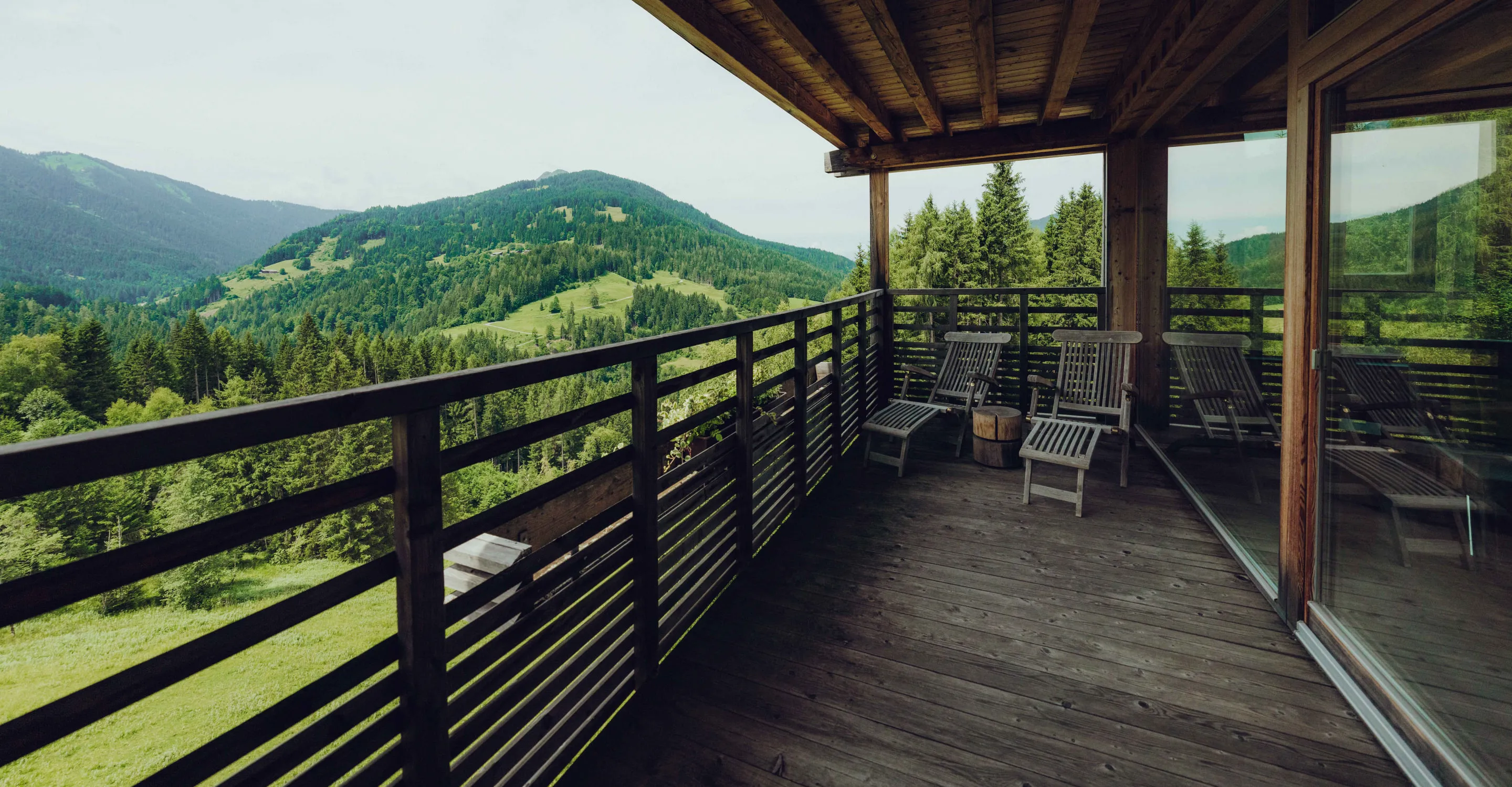 Balkon mit Holzgeländer und Ausblick auf grüne Hügel und Berge