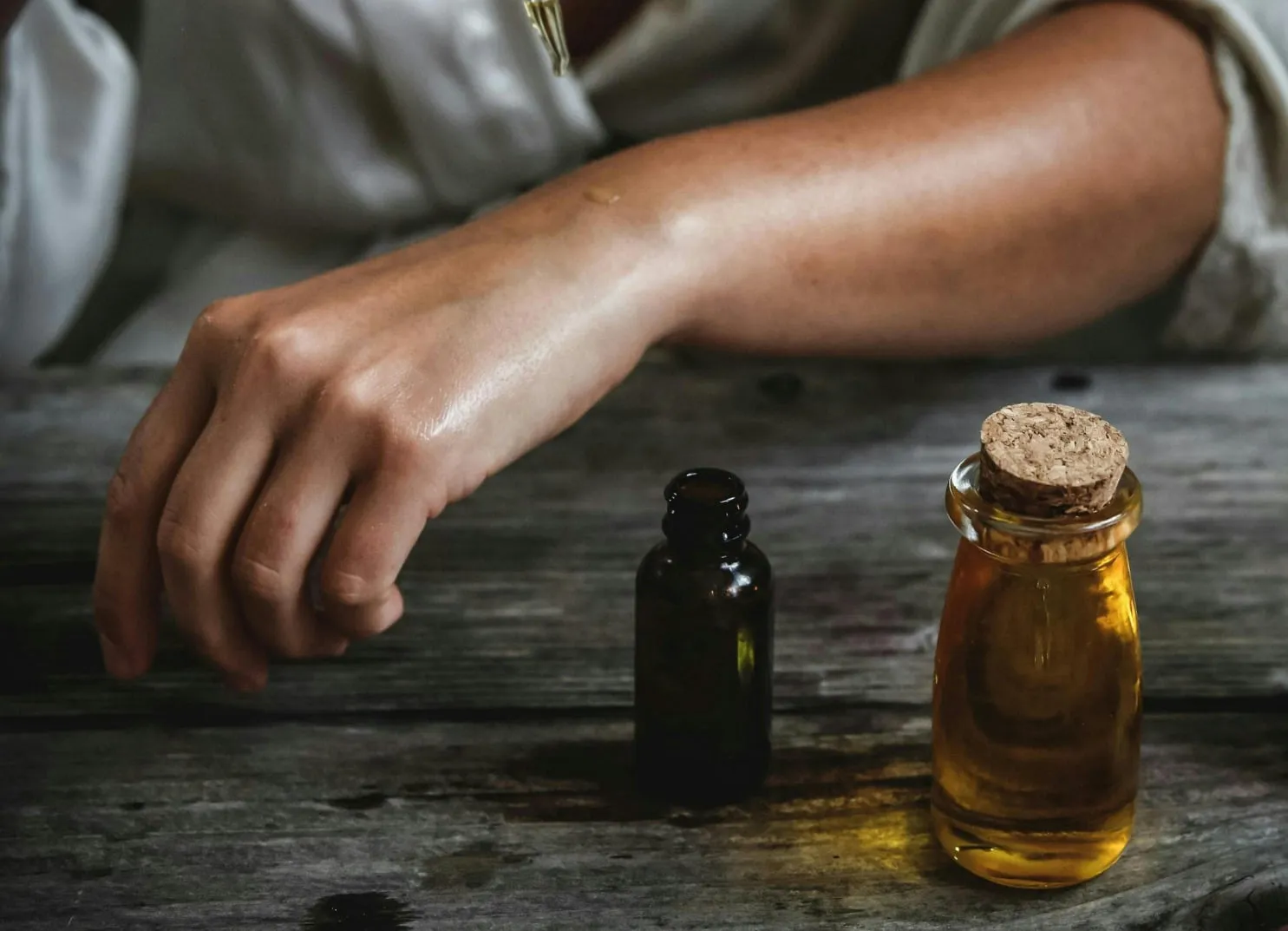 Hand greift nach Glasflasche mit ölähnlichem Inhalt auf Holzoberfläche