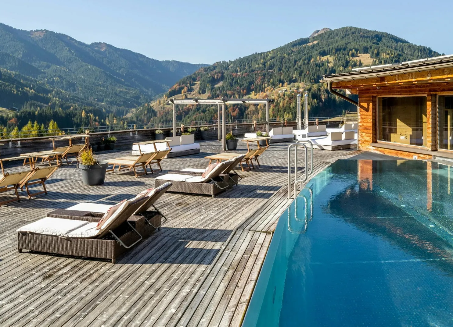 Holzterrasse mit Liegen und Swimmingpool mit Blick auf die Berge