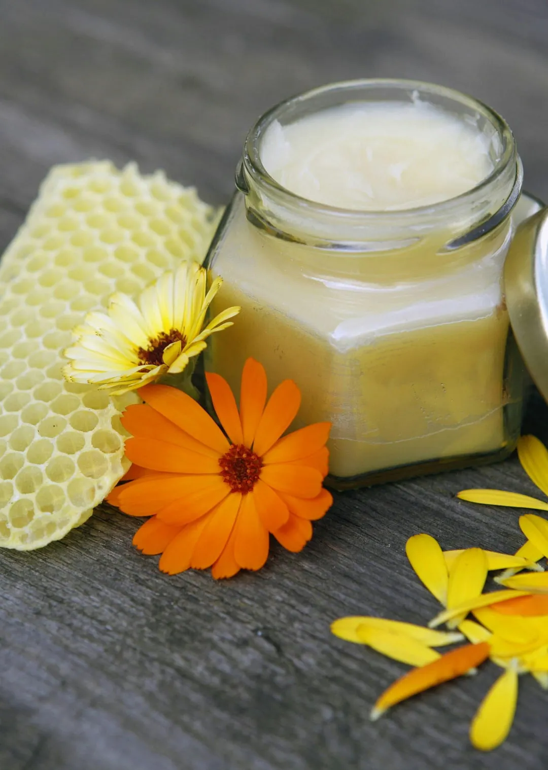 Honigwabe, Glas mit Creme und Ringelblumen auf einer Holzoberfläche