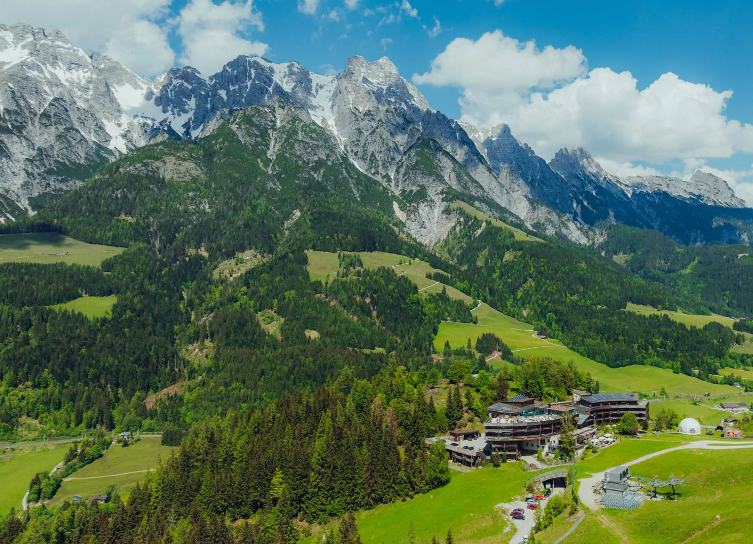 Luftaufnahme vom Holzhotel Forsthofalm in Leogang, umgeben von Bergen und Wäldern
