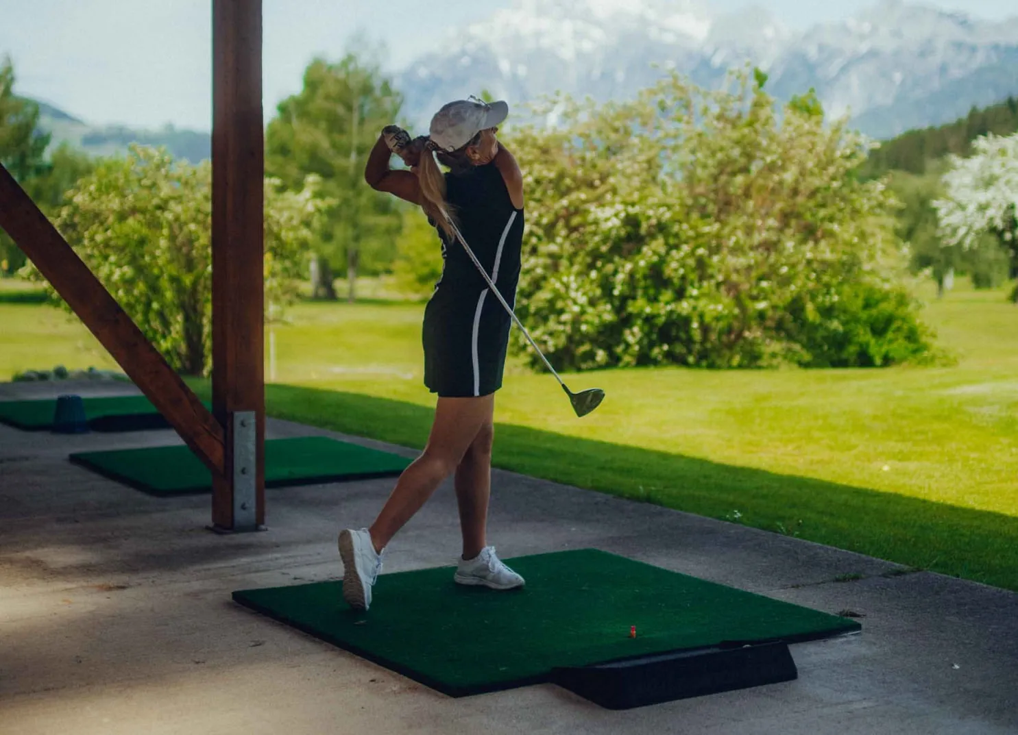 Frau schlägt Golfball auf einer Golfanlage mit Bergen im Hintergrund