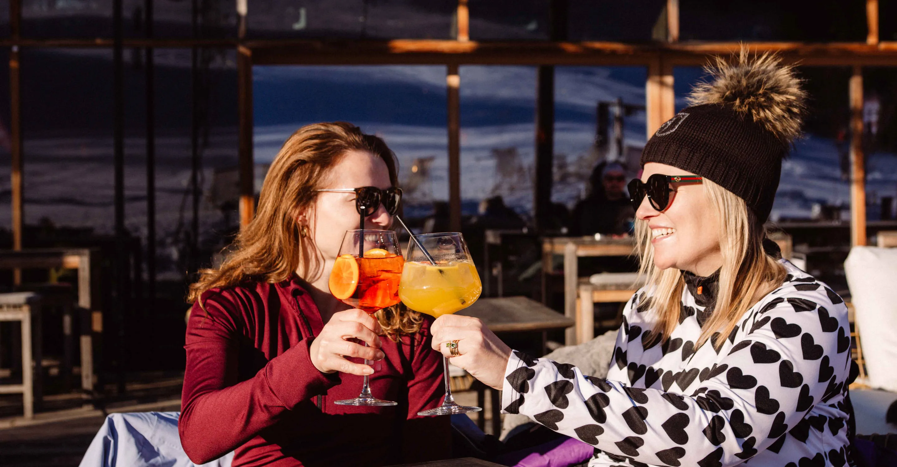Zwei Frauen mit Cocktails auf einer Terrasse, Sonnenlicht und entspannte Atmosphäre.