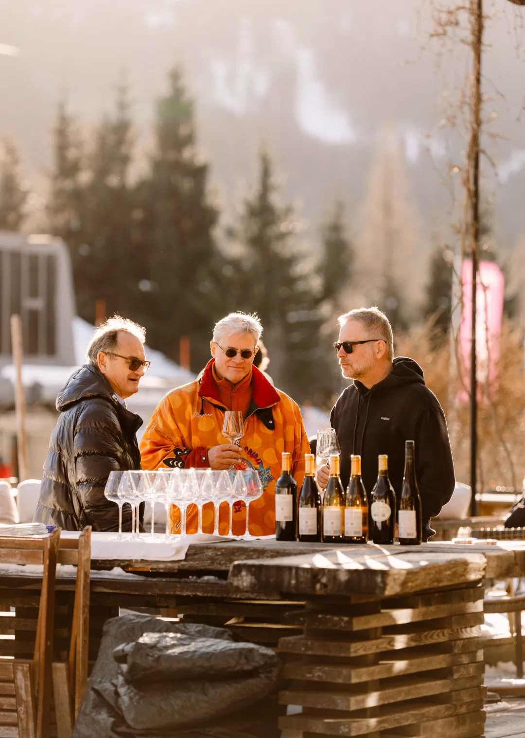 Three people at a table with glasses and wine bottles.