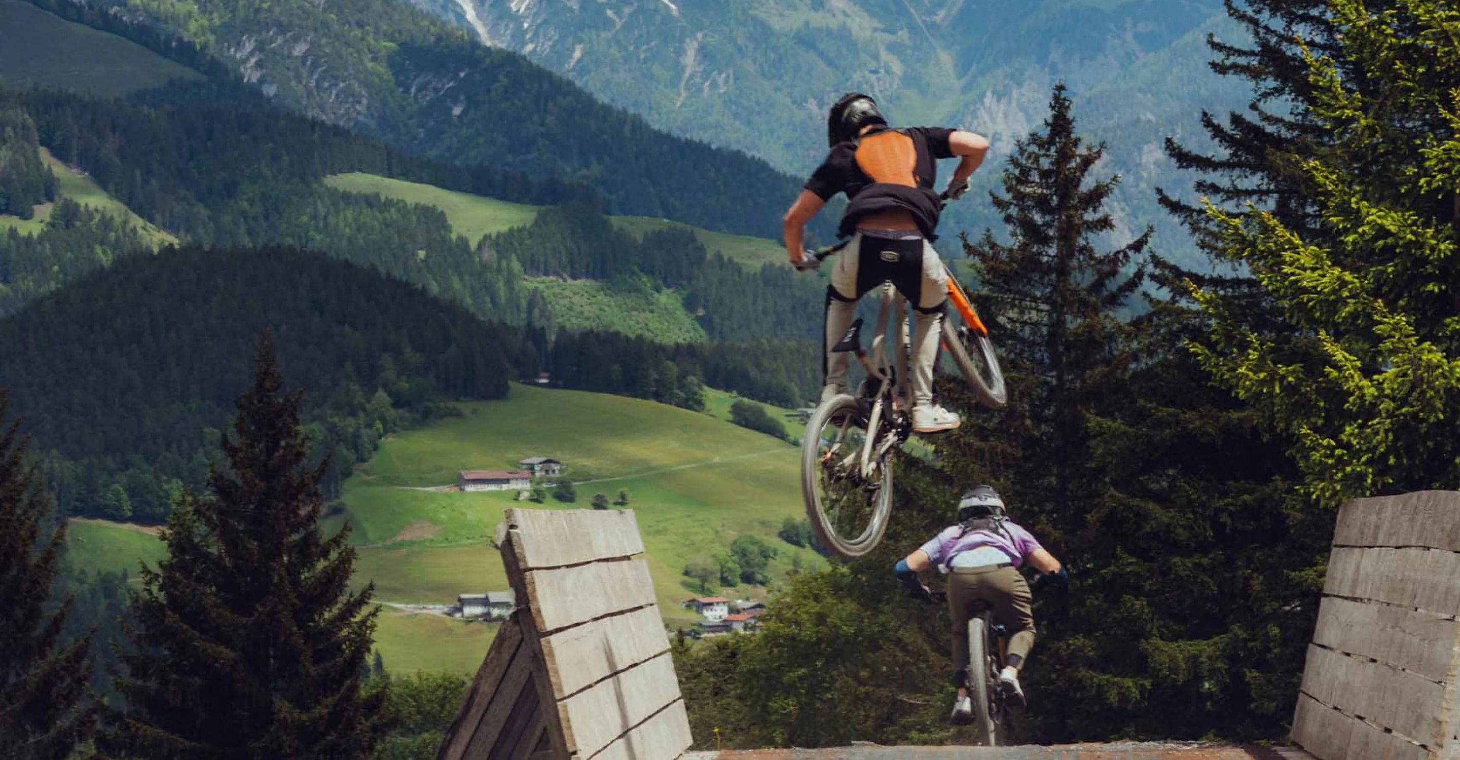 Mountainbiker springen über eine Rampe in den Alpen.
