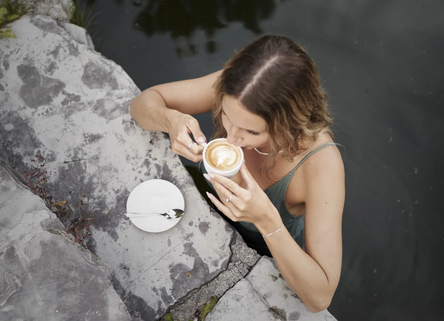 Frau genießt Kaffee am Schwimmteich auf Terrasse.