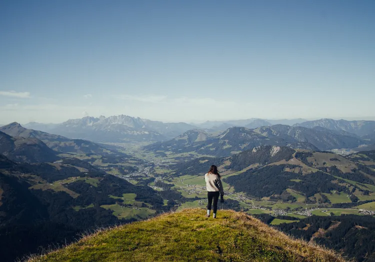 Frau steht auf einem Hügel mit Bergen im Hintergrund